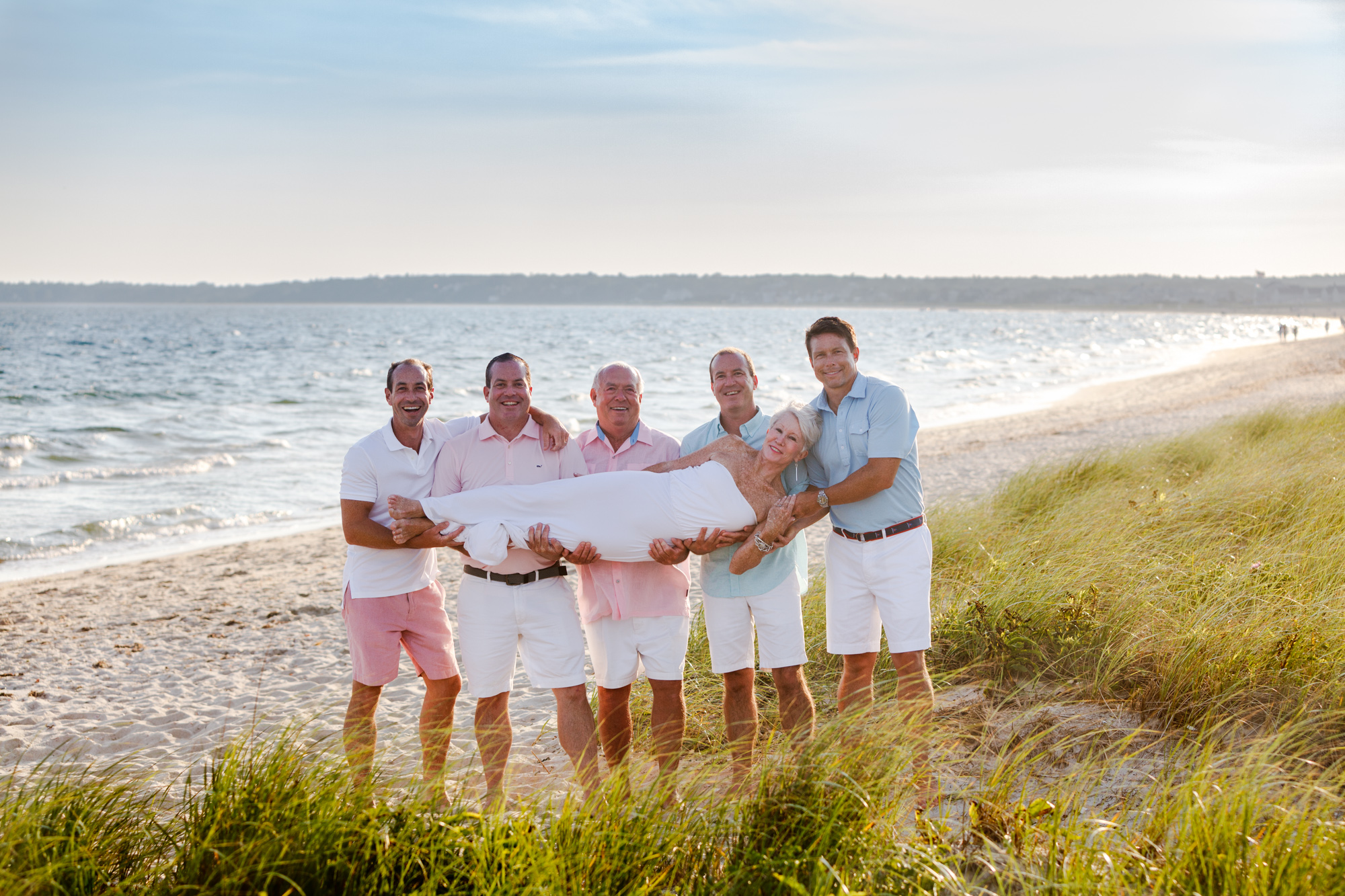 grown sons and dad holding mom sideways on beach