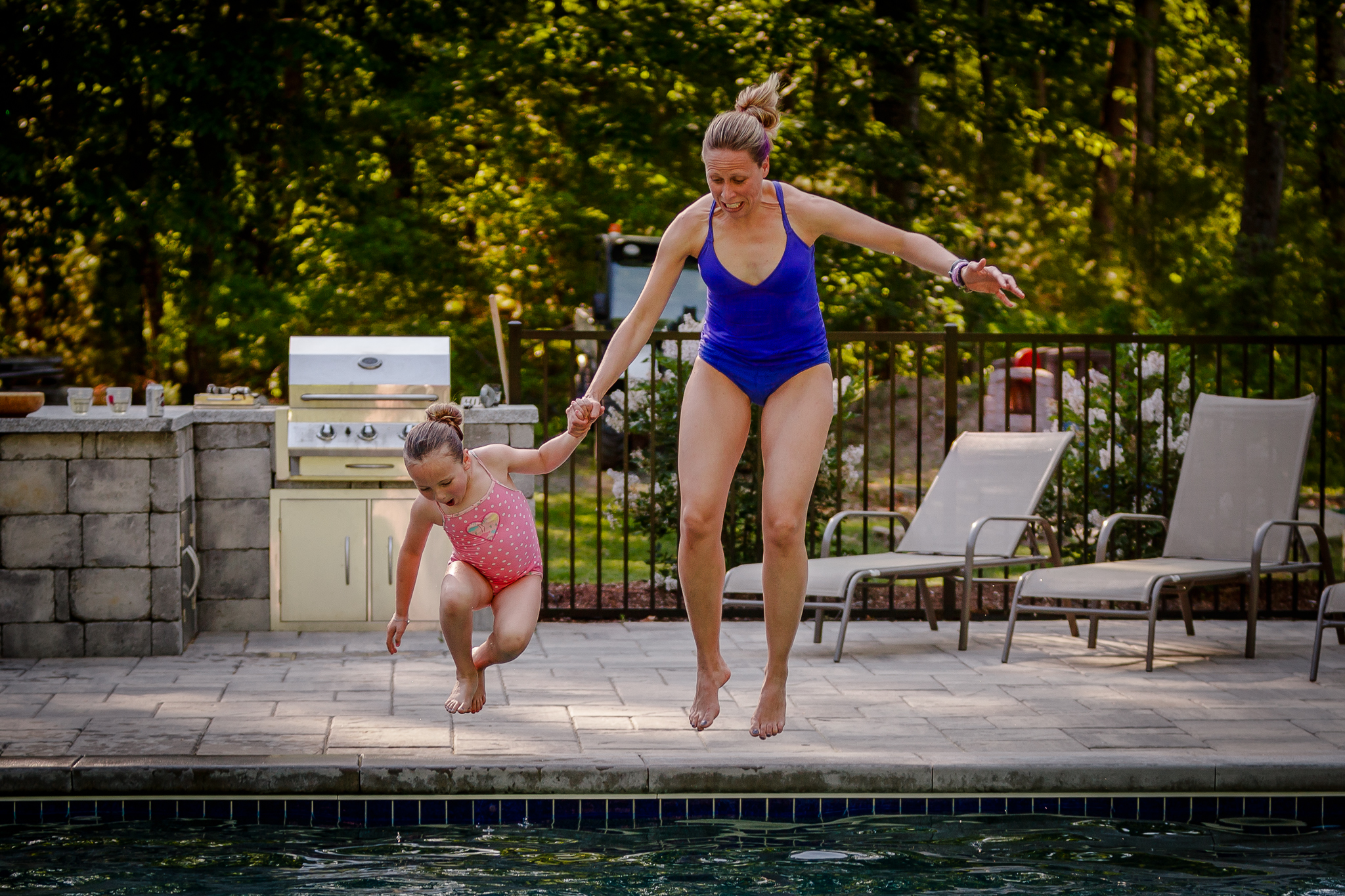 mom and daughter holding hands jumping into pool