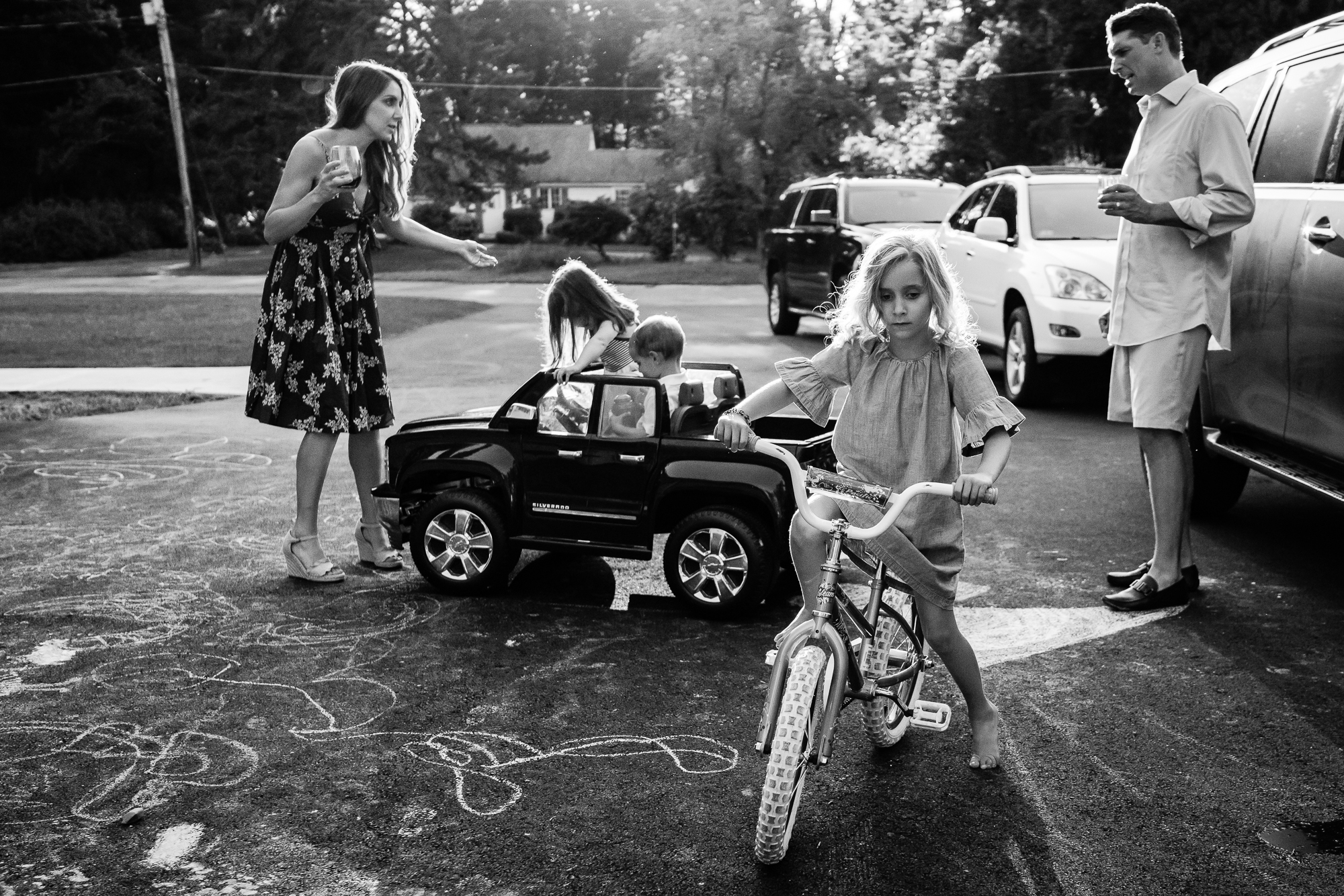 kids in toy car driving into mom holding cocktail and yelling at dad while family plays