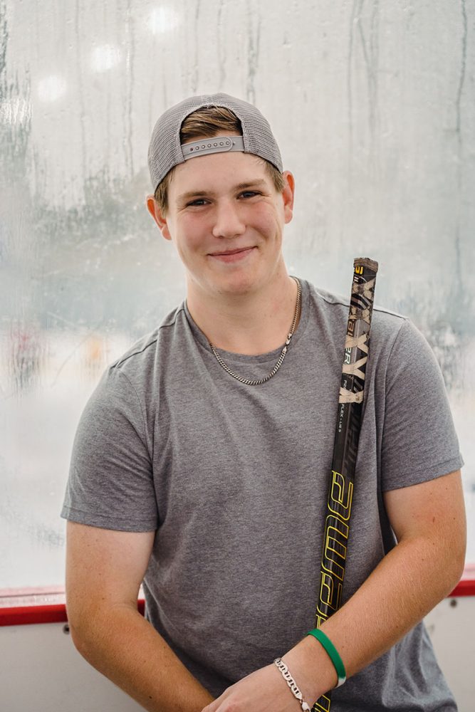 senior boy with wearing backwards baseball hat holding hockey stick
