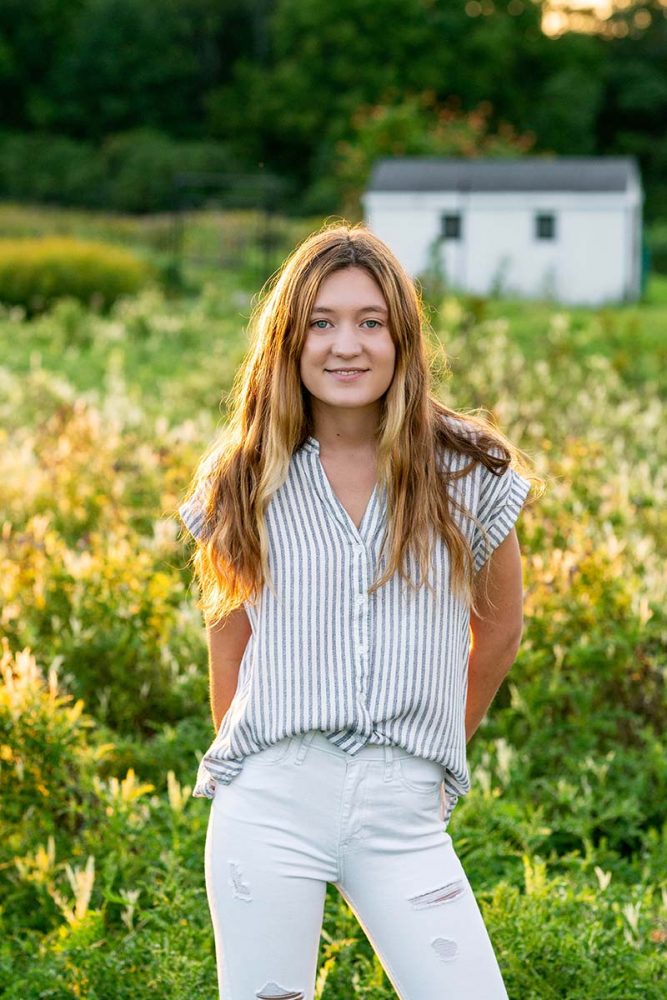senior girl standing in flower field with long brown hair