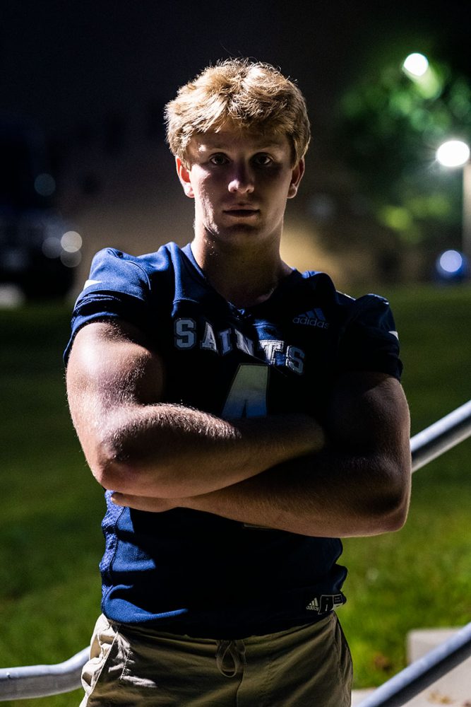 senior boy wearing football jersey standing with arms crossed at night
